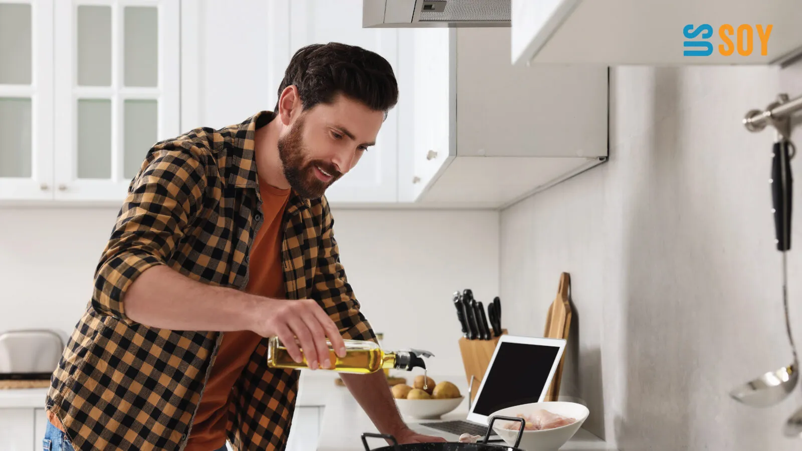 Man cooking at a stovetop while pouring soybean oil from a bottle into a pan in a modern kitchen.